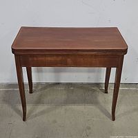 Front view of antique wooden tea table showing wooden top edge and tapered legs.