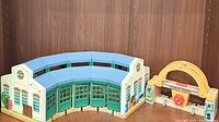 Semi-circular wooden train shed with green doors and white walls and yellow turntable bridge accessory.
