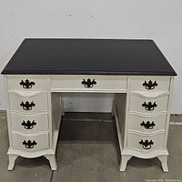 Full front view of the two-toned wooden desk with 8 drawers, showing dark top and white base with ornate metal handles.
