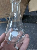 Close-up of hand holding a 250ml Pyrex clear glass Erlenmeyer flask with white measurement markings and model number printed.
