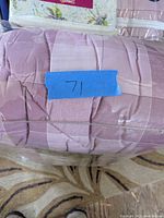 Photo of pink plaid comforter wrapped in plastic with a blue tape label '71'