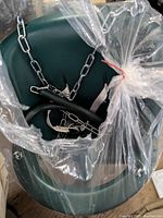 Photo showing top view of green plastic children's seat swing inside clear plastic packaging, with attached metal hanging chains coiled inside.