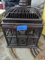 Front view of the wooden decorative cage showing the square base, vertical bars, and the domed top with a round wooden finial.