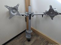 Dual monitor mount arm with two VESA mounting plates and clamp base for mounting on desk.
