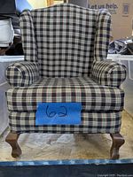 Front view of the doll chair showing its plaid upholstery and wooden cabriole legs, with a blue label '62' on the front.