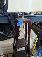 Front view of wooden A-frame floor lamp with shelves and white fabric shade shown at approximate 6 feet height.