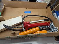 Red hydraulic pump with hose and orange hydraulic ram in cardboard box
