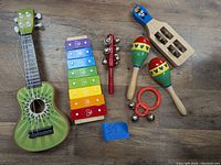 Overview of all the items laid on floor showing ukulele, xylophone, tambourine stick, castanet, maracas, and jingle bells