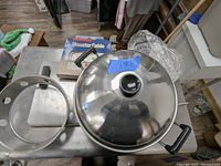 Photo showing stainless steel wok with lid, placed on a metal cart alongside Monster Cable box