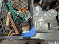 Photo showing the caulk guns, steel brush, glass canisters, and metal crate containing the lot items