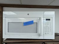 Front view of white GE over the range microwave showing control panel and handle, with a blue tape marked '30'.