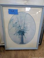 Oval botanical artwork with blue-toned leaves and branches in gray frame