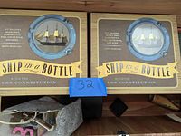 Two boxed Ship in a Bottle kits displayed side by side. Each box has a porthole window showing the model ship inside and branded with Kaplan Murphy Co.