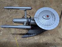 Top-down photo of the silver USS Enterprise model phone resembling the starship NCC-1701 with visible markings on the saucer section.