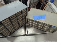 Two metal storage drawer systems with small clear plastic drawers, labeled with various hardware part types and sizes, placed on a metallic surface.