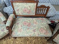 Front angled view of Victorian settee showing floral-patterned upholstery on seat, backrest, and armrests, with wooden frame and carved detailing.