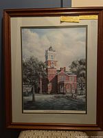 Framed art print showing the original Gwinnett County Courthouse with detailed architecture and surrounding greenery, visible pencil signature and numbering on bottom right, double matting, and brown wooden frame.