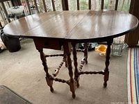Front and side view of the antique gateleg table with both leaves extended showing wood finish and turned legs.