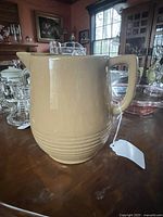 Side angle view of the beige stoneware jug with handle and spout, showing overall shape and size in room setting.