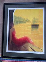 Full view of the framed seriolithograph showing a woman in a red dress sitting on a bench by the water with golden background, signed lower right.