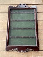 Full view of the vintage mahogany spoon rack showing its rectangular frame, decorative carved scrolls on top and bottom, four horizontal rows with slots, and green felt backing.