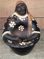 Front view of black and brown Chulucanas pottery woman figurine with white dot pattern on chest and rounded form