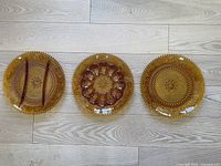 Set of three 12 inch amber glass serving plates in Tiara Sandwich pattern, including deviled egg plate, divided sandwich plate, and serving plate.