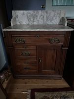 Full front view showing the marble top, backsplash, wooden cabinet base with multiple drawers and cabinet door, brass handles.