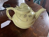Side view of vintage yellow Hall-USA teapot with floral and leaf decoration, showing handle and spout.