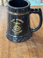 Full view of vintage black ceramic mug with yellow lettering and emblem on front.