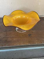 Side angle of yellow vintage Italian blown glass bowl with ruffled edge on wooden surface
