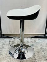Side view of new black and white bar stool showing curved plastic seat and chrome pedestal base with footrest.