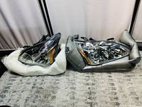 Pair of car headlights placed on grey carpet, each wrapped in protective foam.