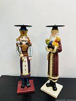 Front view of the two Noisette figures - Nutcracker King and Santa Claus, both with candle holders attached on top, standing on square bases