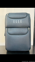 Full front view of large black ELLE suitcase with two front zippered compartments and ELLE logo printed on upper pocket.