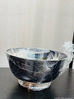 Photo of larger silver colour metal bowl wrapped in plastic wrap, showing reflective metal surface and rounded shape.