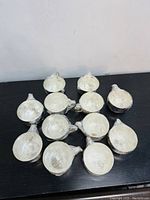 12 small silver bowls with a handle, all wrapped in plastic appear to be part of a matching set.