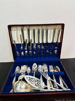 Full view of the silver plated flatware set displayed in blue velvet-lined wooden case showing knives, forks, spoons and serving utensils.