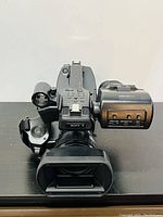 Front angle of camcorder showing lens hood, zoom/focus assembly, viewfinder on right