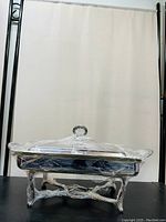 Front view of vintage silver rectangular covered fire baking serving dish wrapped in protective plastic, showing ornate base and lid with handle.