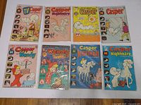 Top-down photo showing eight vintage Casper the Ghost comic books from the 1970s, arranged in two rows of four on a wooden floor.