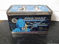 Photo of metal tin container with Star Wars A New Hope Series 1 artwork featuring Luke Skywalker, R2-D2, C-3PO, and X-Wing fighter. Tin is rectangular with hinged lid.