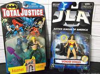 Photo shows both Aquaman and Wonder Woman action figures in original unopened packaging, front view.