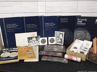 Full lot showing 5 Whitman coin folders standing upright, assorted loose and carded coins, penny rolls, and coin guides on a flat surface