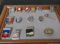 Photo showing a display board with 15 pins including Soviet statues, Lenin profiles, city badges, and emblems of USSR and CCCP.