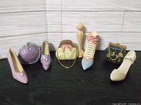Full view showing all 8 decorative shoes and handbags arranged on a black surface against a white paneled background.