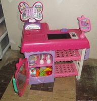 Front view of the pink and purple Minnie Mouse market cash register with open cabinet door showing food items inside.