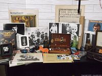 Wide view of all lot items including pins, tie tacks, VHS tape, magazines, photographs, small collectibles and wooden plaque.