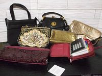 Full lot showing seven items: structured black leather handbag, black rounded monogram handbag, gold croc-embossed clutch, floral needlepoint clutch, gold mesh clutch, burgundy shiny clutch, and red zip pouch with contents.