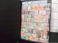 Black album page filled with multiple rows of vintage stamps in various colors and denominations, many with postmarks.